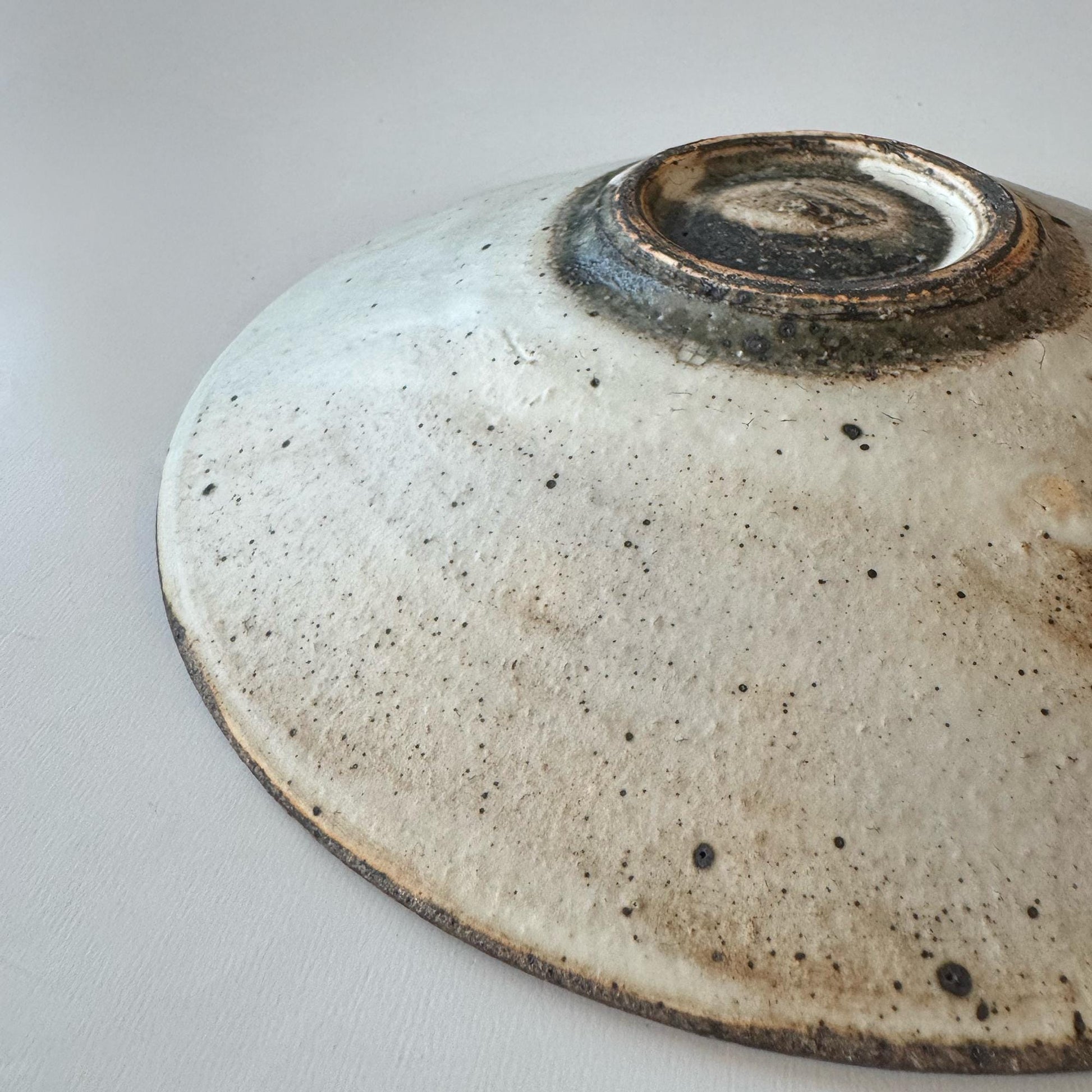 A handcrafted, shallow ceramic bowl with a subtle, earthy tone and a speckled glaze, evoking a sense of understated beauty.