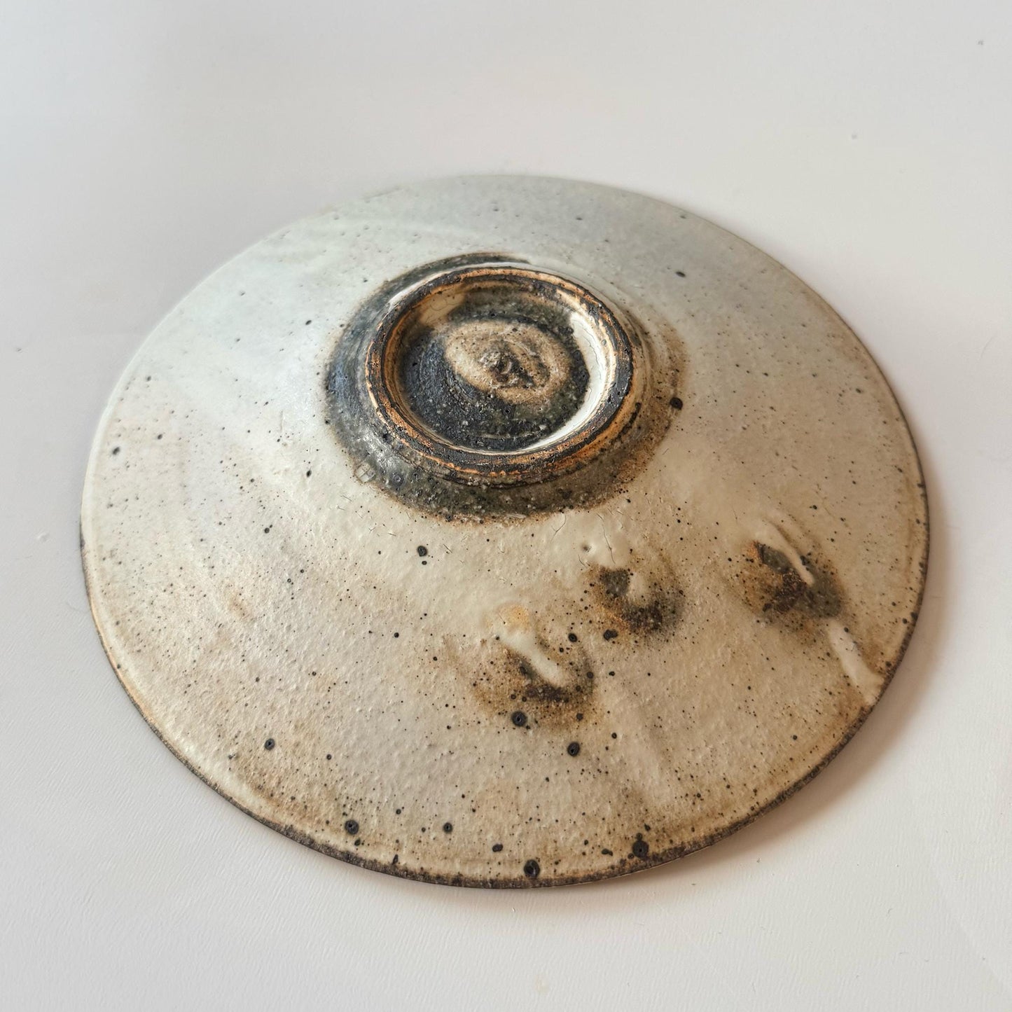 A handcrafted, shallow ceramic bowl with a subtle, earthy tone, created by Japanese artisan Takashi Sogo.