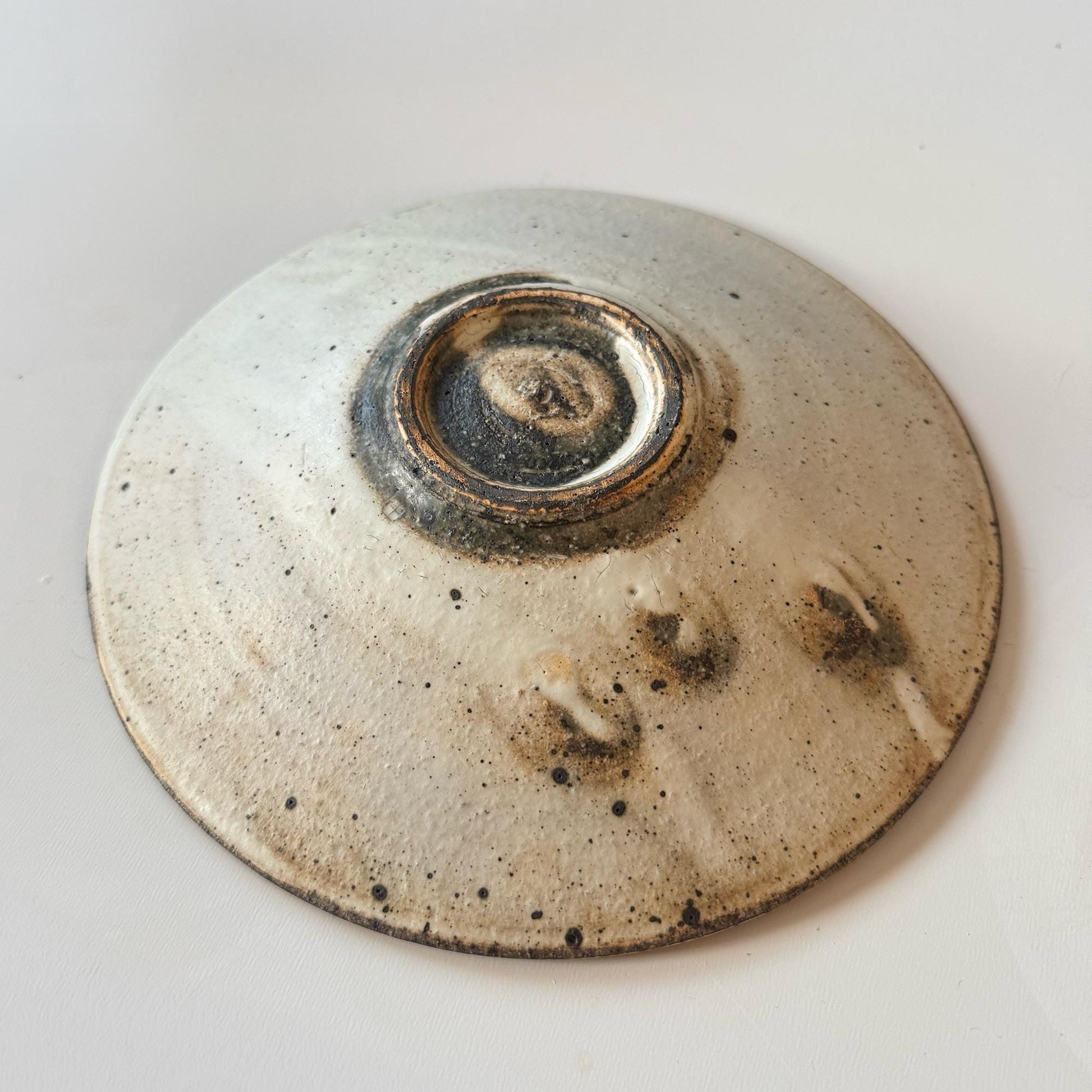 A handcrafted, shallow ceramic bowl with a subtle, earthy tone, created by Japanese artisan Takashi Sogo.