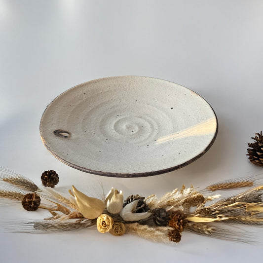 A handcrafted, shallow ceramic bowl with a subtle, earthy tone and a delicate, speckled glaze.