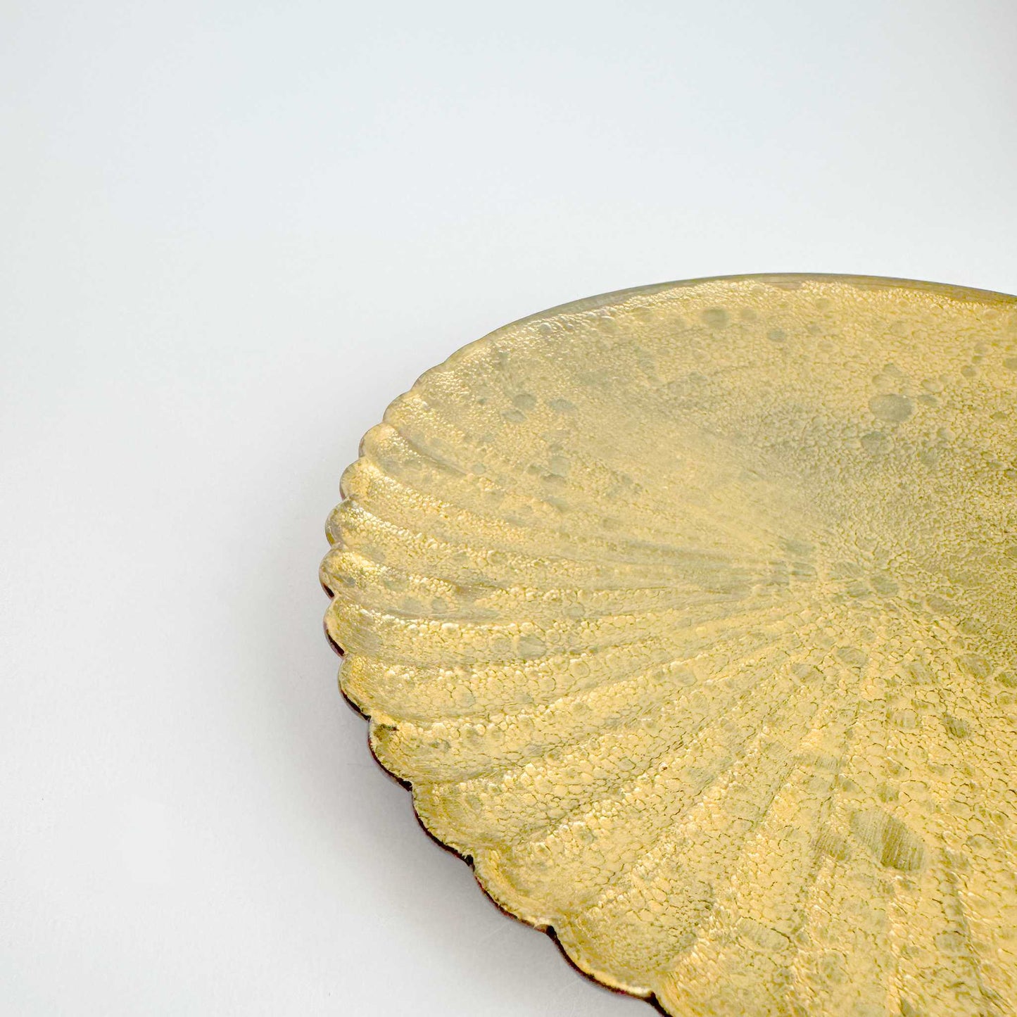 Close-up of a gold decorative plate with scalloped edge on a white background