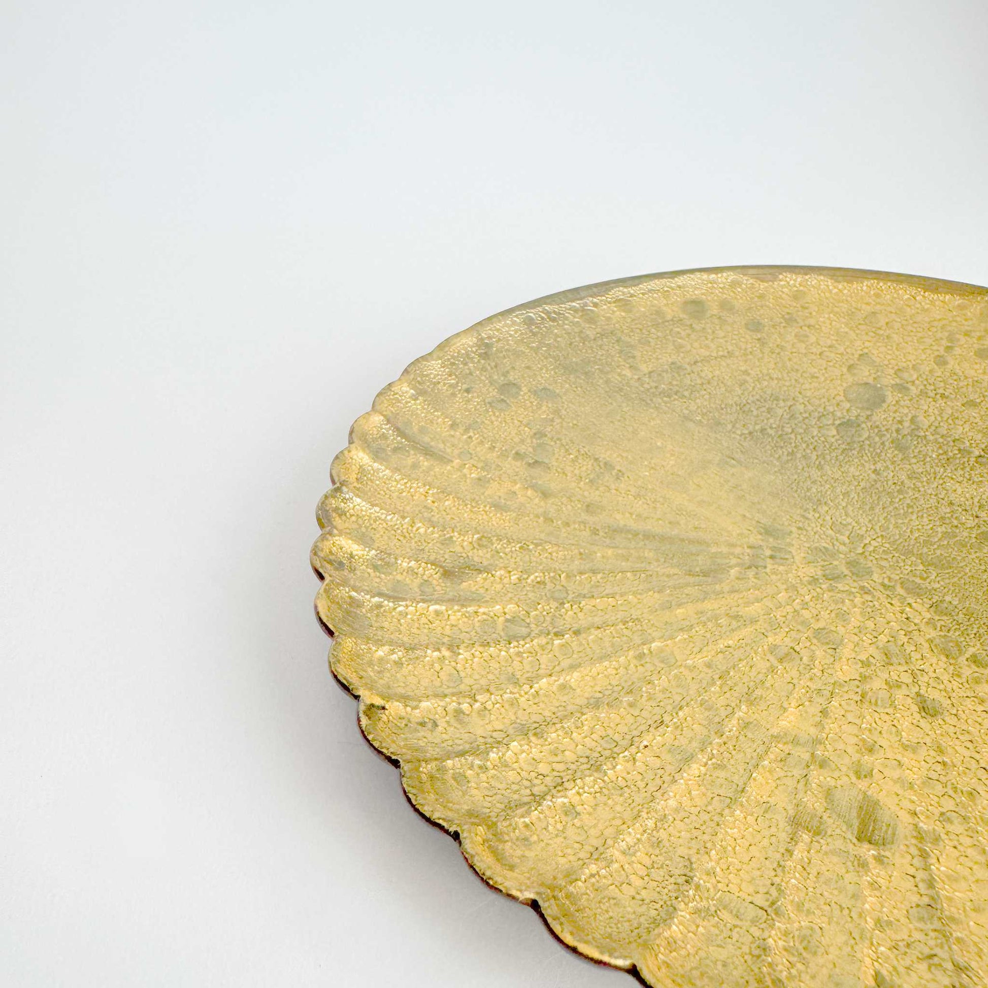 Close-up of a gold decorative plate with scalloped edge on a white background