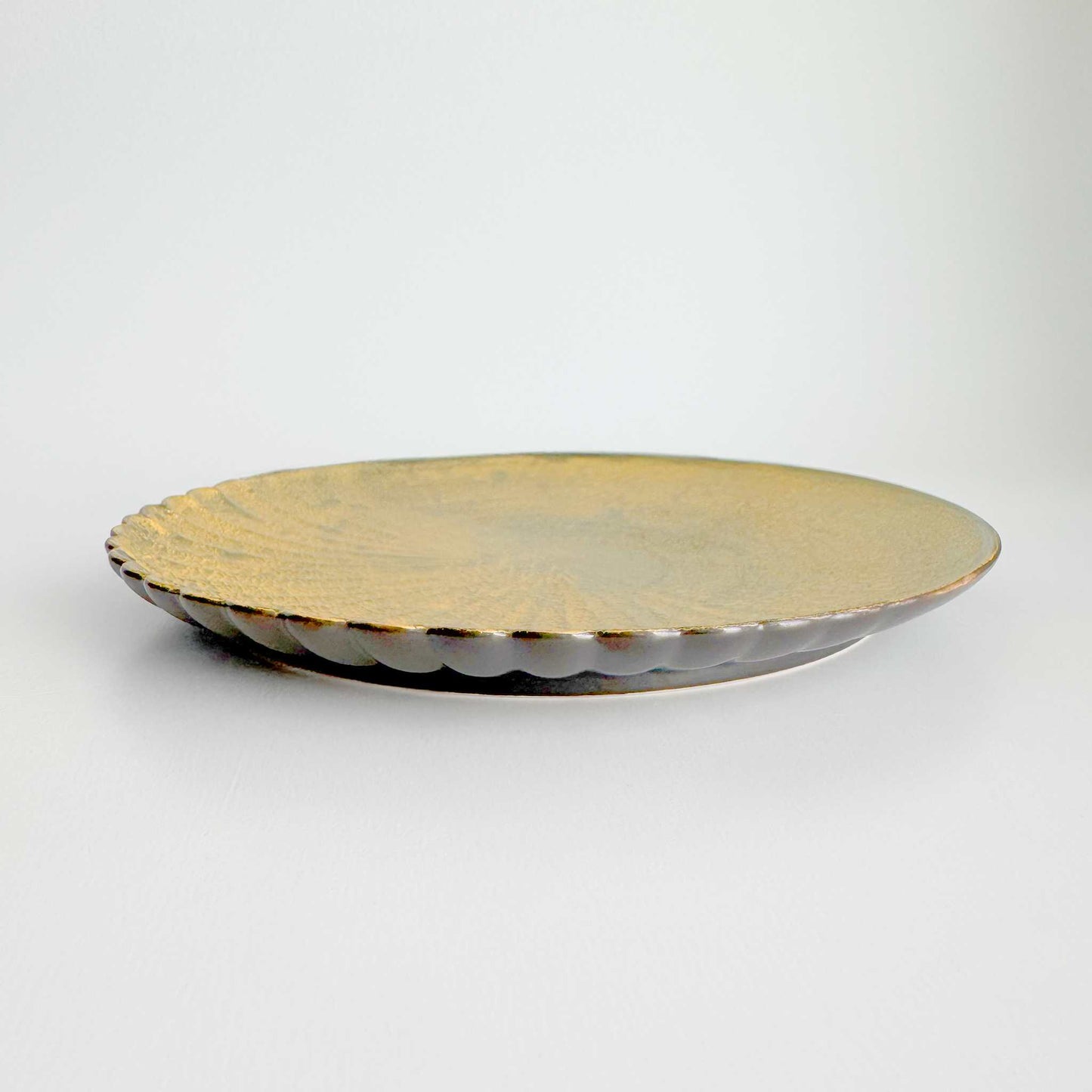 Round metallic plate with scalloped edge on a light gray background