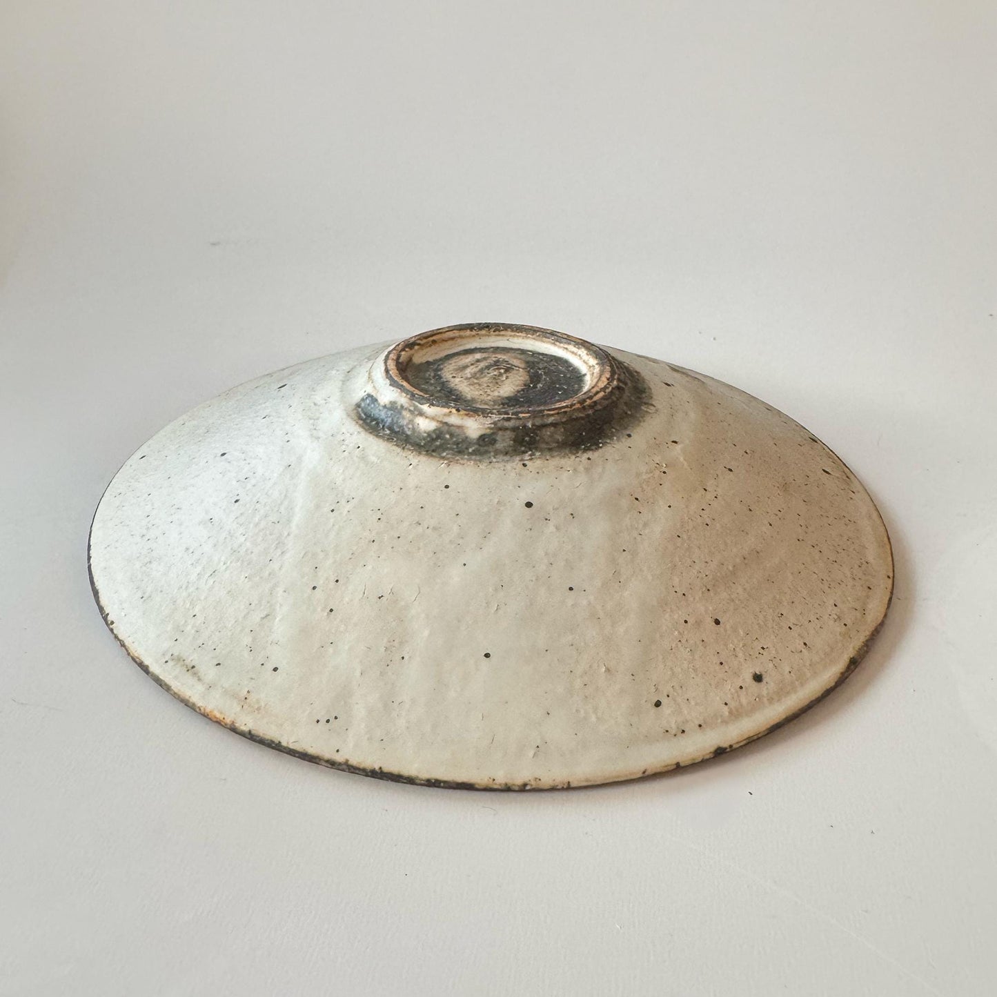 A handcrafted, shallow ceramic bowl with a unique, speckled glaze, created by Japanese artisan Takashi Sogo.