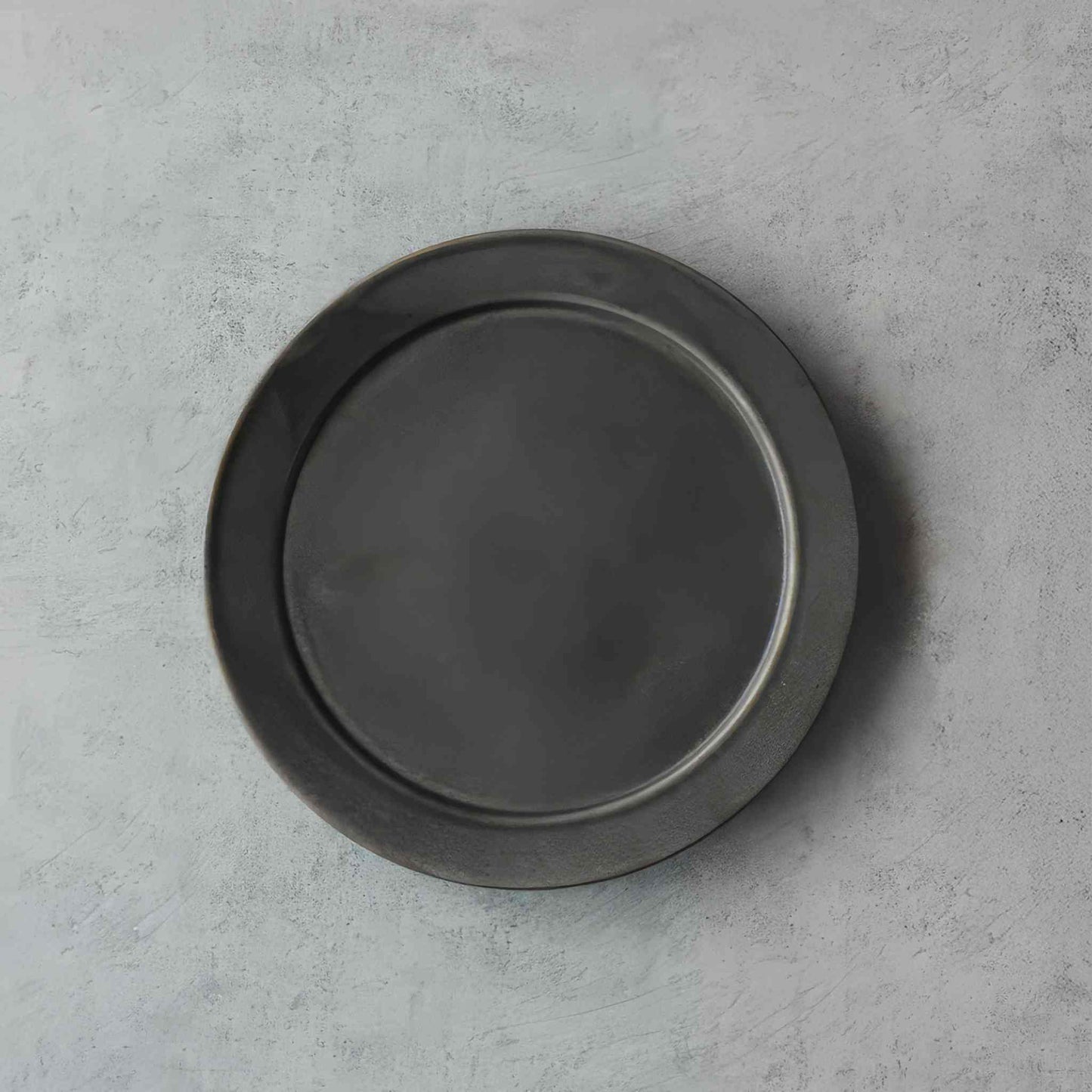 A small, black, handcrafted plate with a subtle, organic glaze, set against a neutral background.