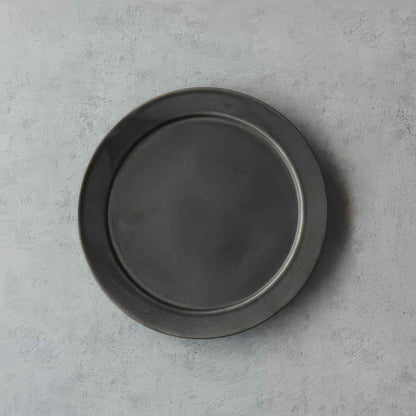 A small, black, handcrafted plate with a subtle, organic glaze, set against a neutral background.