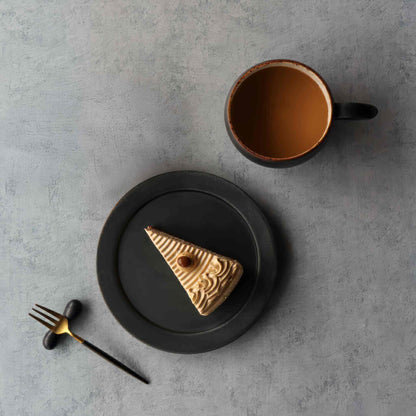 A small, handcrafted plate with a black and white glaze, featuring intentional imperfections and an organic, natural look.