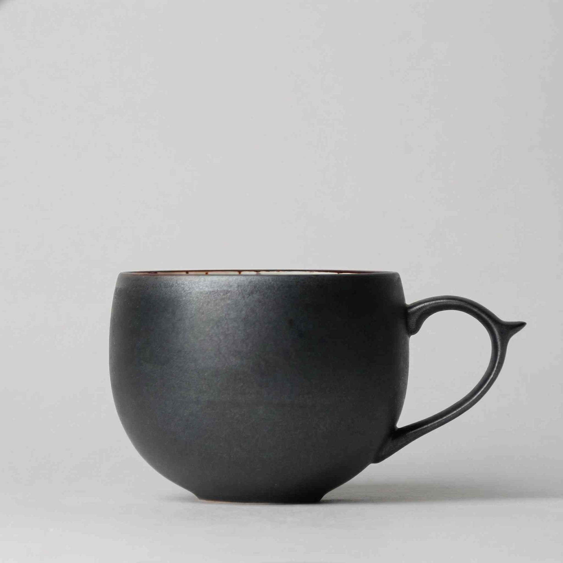 A black, handcrafted, wabi-sabi-inspired ceramic mug with a saucer, made in Arita, Japan.