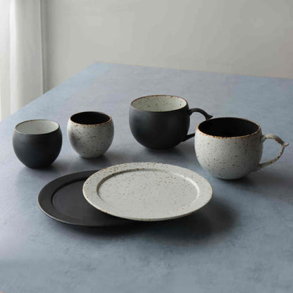 A small, handmade plate with a black and white speckled glaze, sitting on a table.