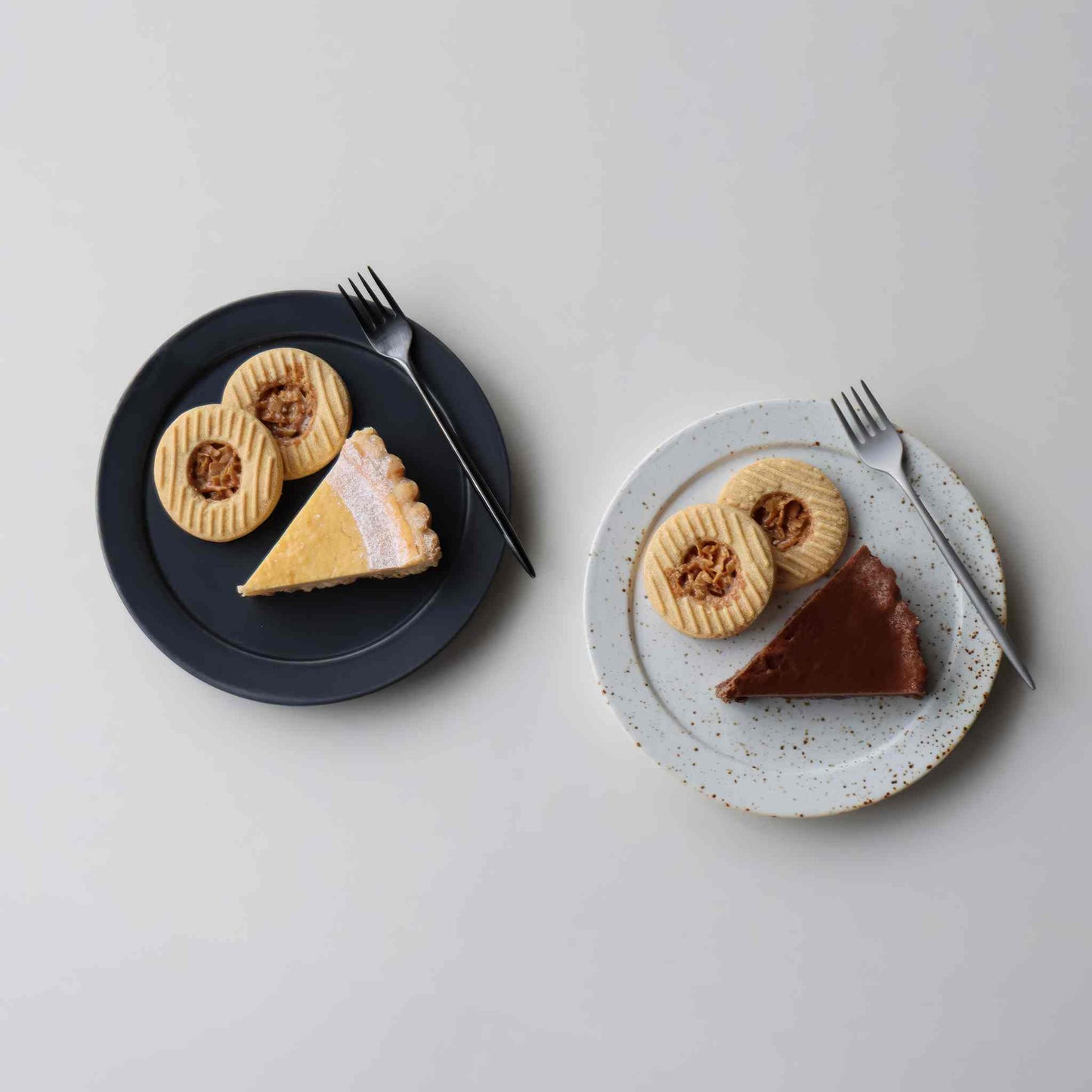 A small, handcrafted plate with a black and white speckled glaze, served with a fork and two types of pie.