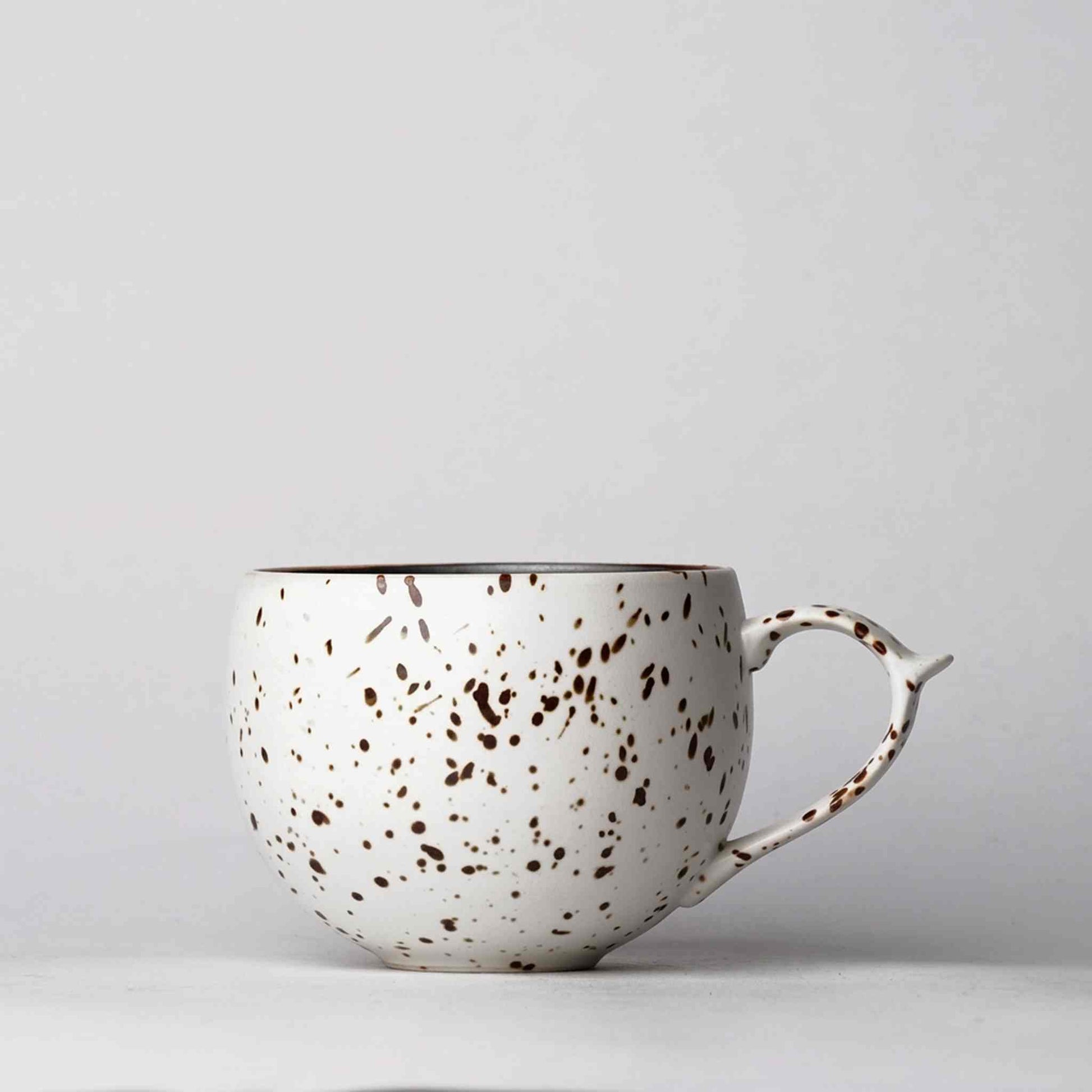 A white, speckled, handcrafted ceramic mug with a handle, set against a plain white background.
