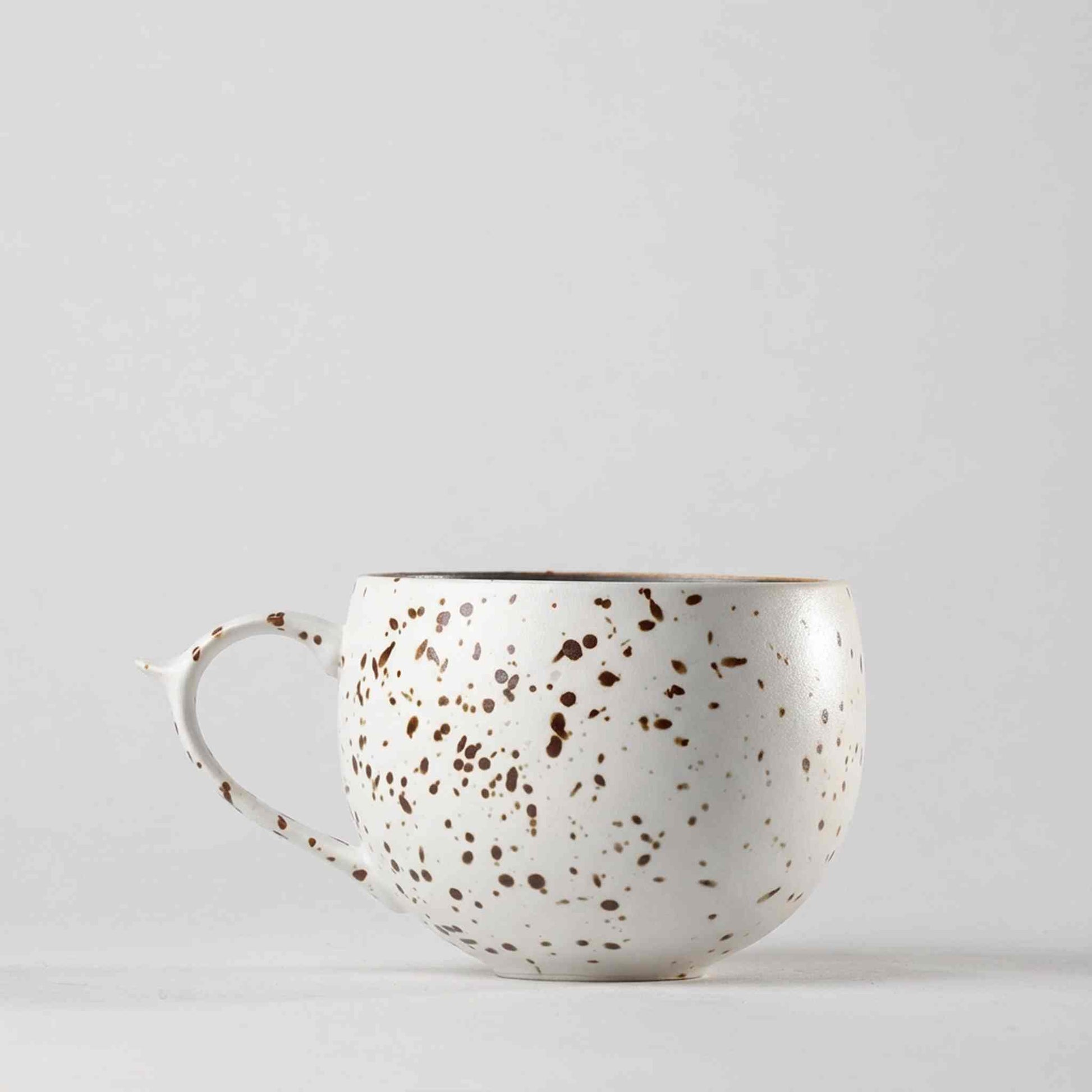A white ceramic mug with a speckled gold and brown design, set against a plain white background.