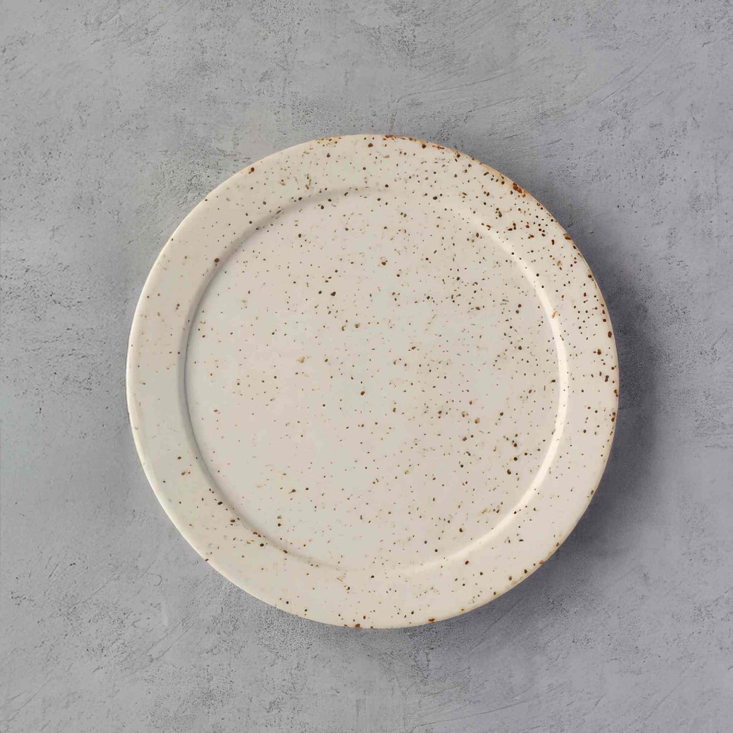 A small, handcrafted plate with a speckled, earthy glaze, evoking the Japanese concept of sabi, where imperfections are celebrated.
