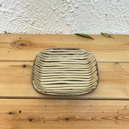 Handmade slipware square plate with unique, hand-applied surface patterns in a neutral, earthy tone, set on a natural wood surface.