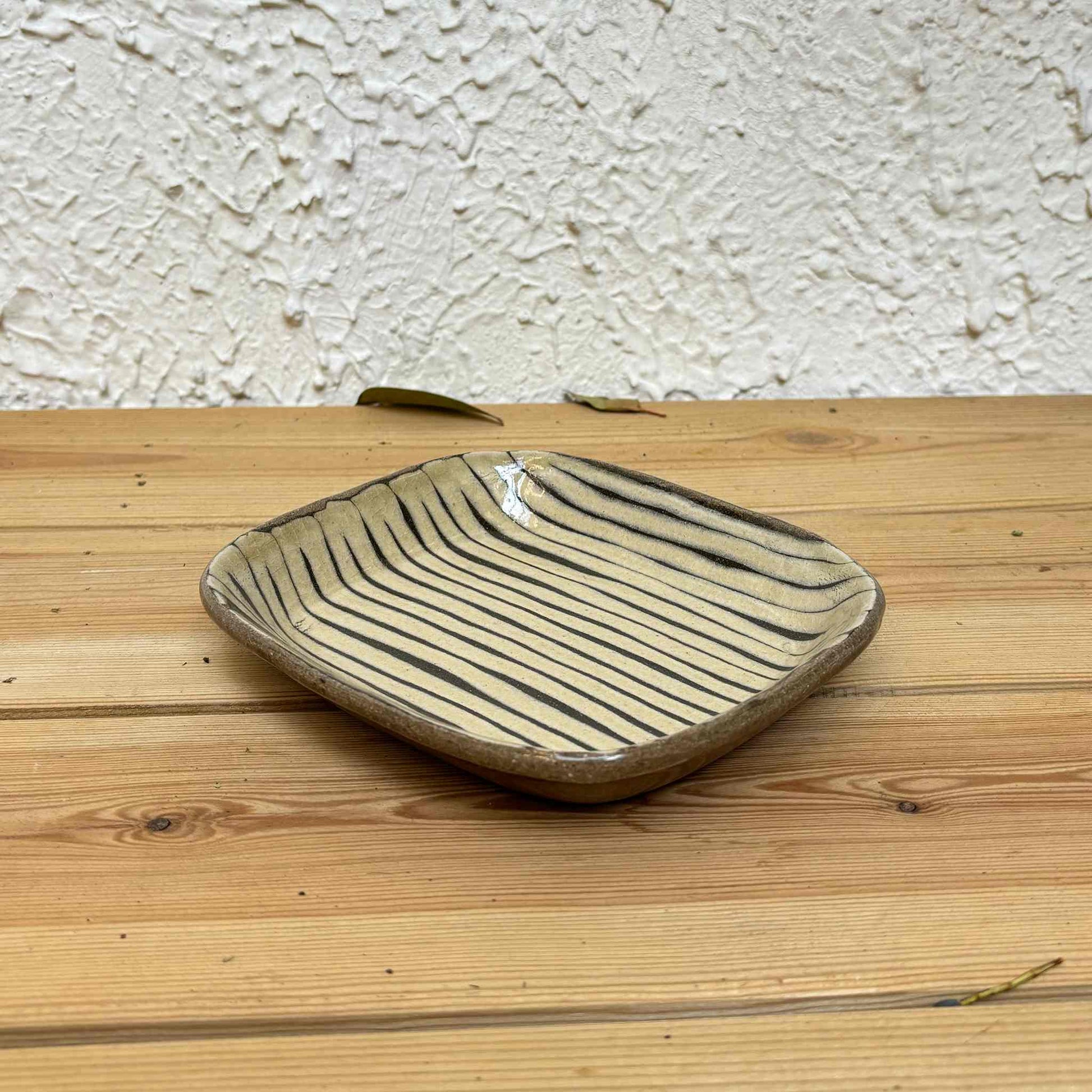Handmade square plate with unique, hand-applied surface patterns in a natural, earthy tone, set on a wooden surface.