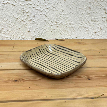 Handmade square plate with unique, hand-applied surface patterns in a natural, earthy tone, set on a wooden surface.