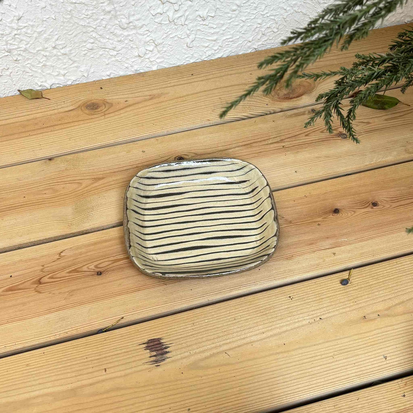 Handmade slipware square plate with unique, hand-applied surface patterns in a natural, earthy tone, set on a wooden surface.