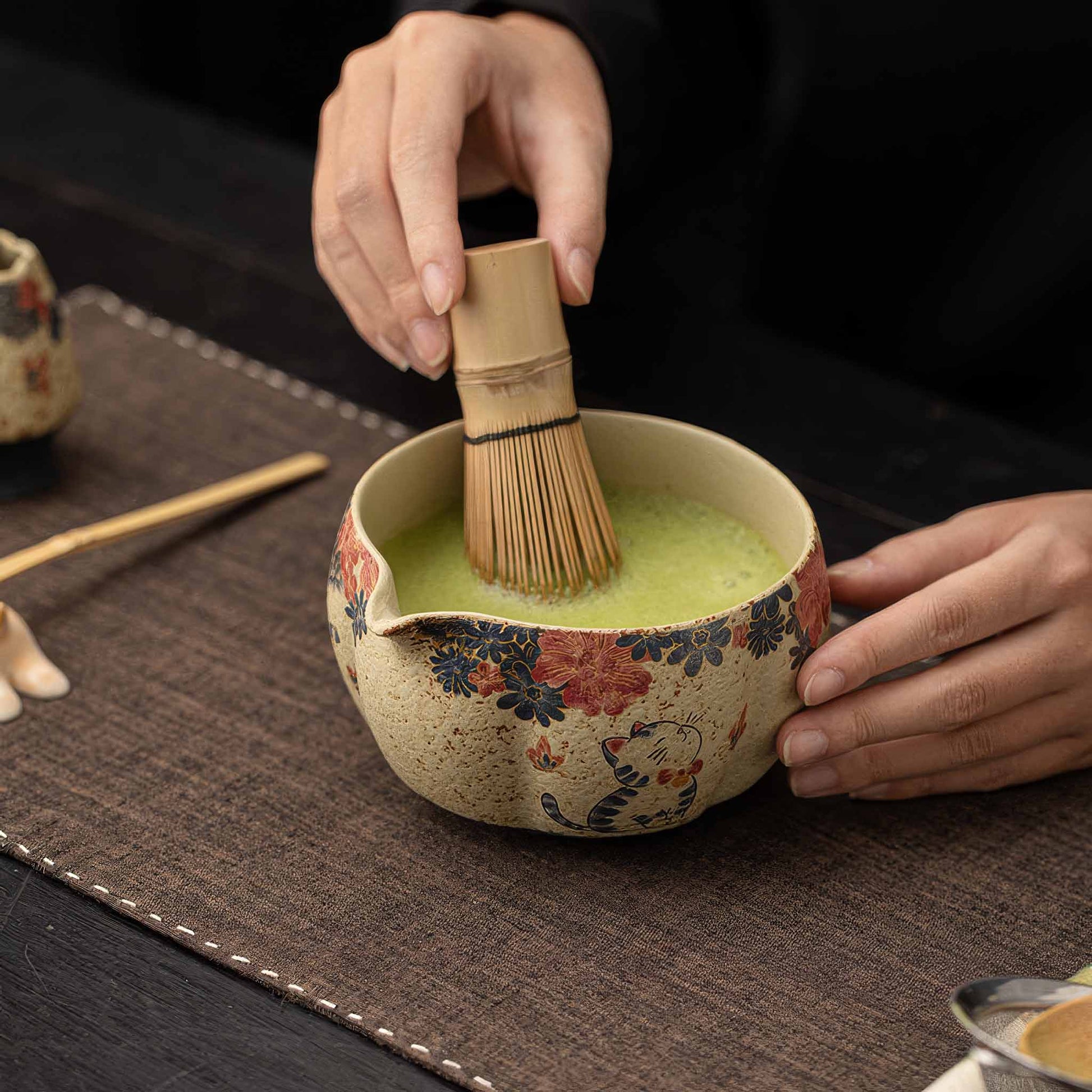 A person's hands hold a blue and white flint red matcha bowl, filled with a vibrant green matcha tea, on a dark brown table.