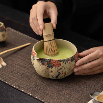 A person's hands hold a blue and white flint red matcha bowl, filled with a vibrant green matcha tea, on a dark brown table.