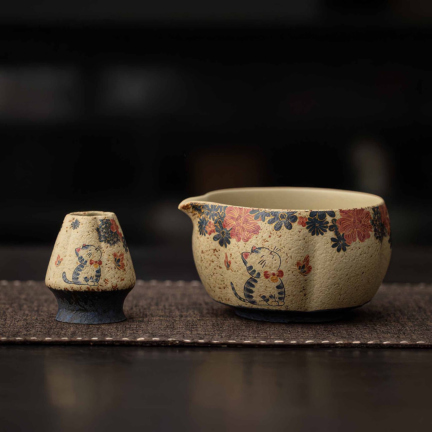 Hand-painted blue and white flint red matcha bowl set with whisk and scoop on a dark woven mat.