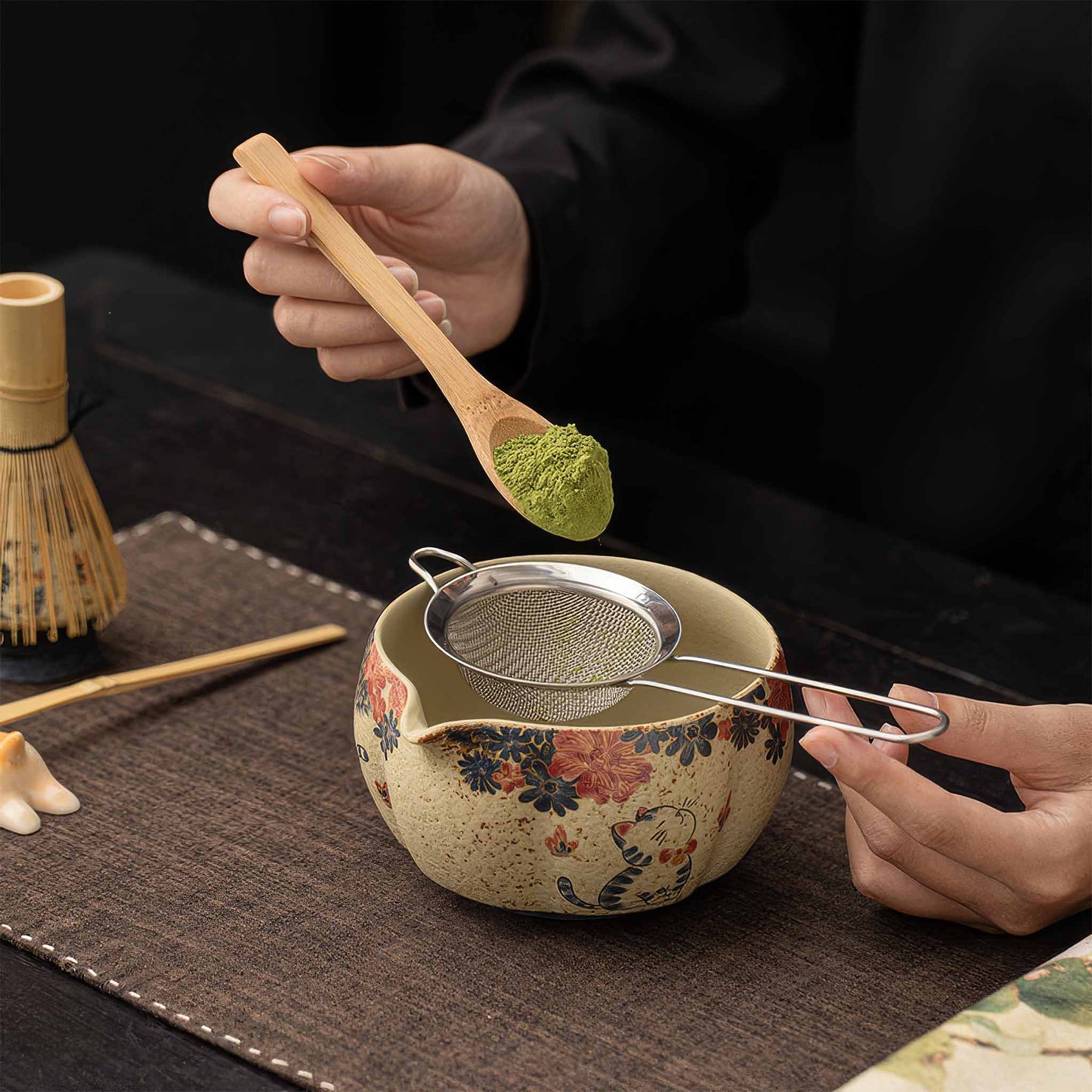 A person's hands hold a traditional Japanese matcha bowl, made of blue and white flint red ceramic, on a dark wooden table.