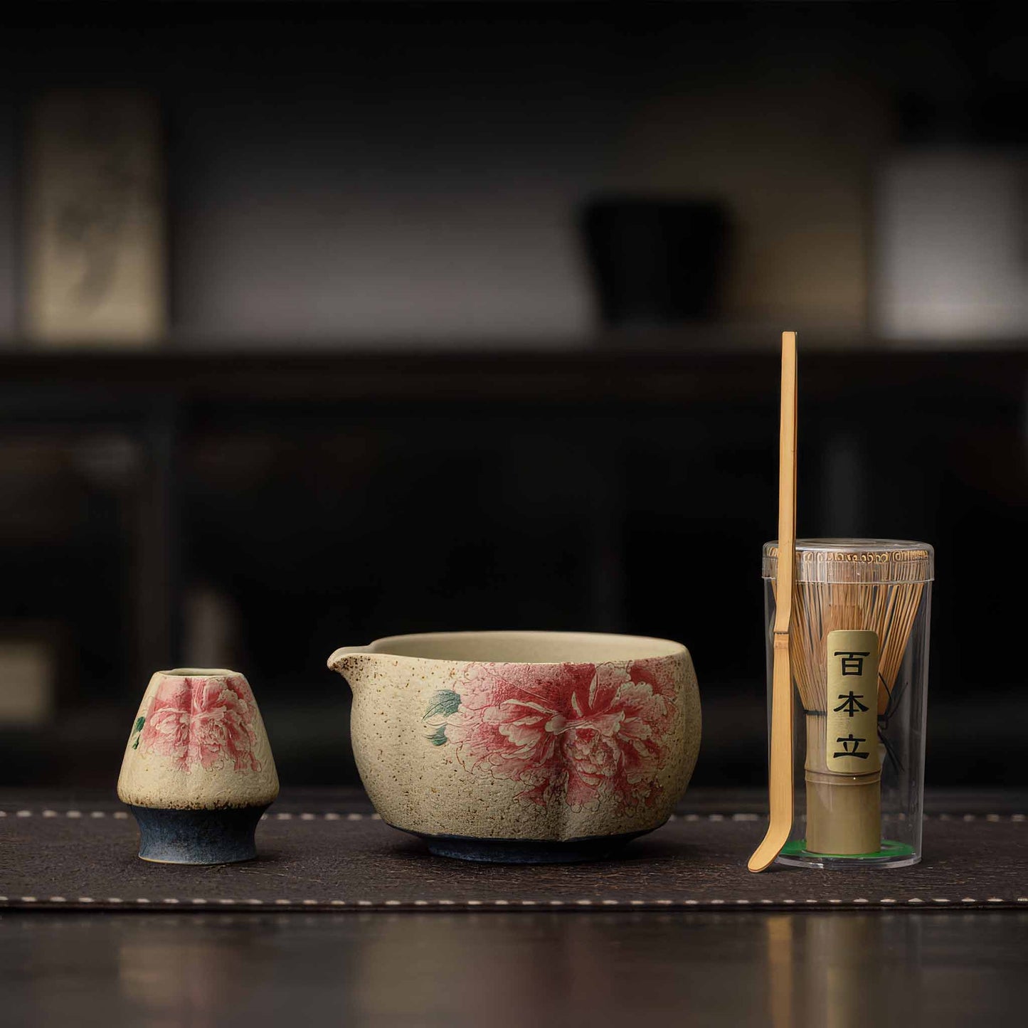 A Handcrafted matcha bowl set with a bamboo whisk and a matcha scoop, set on a dark wooden table.