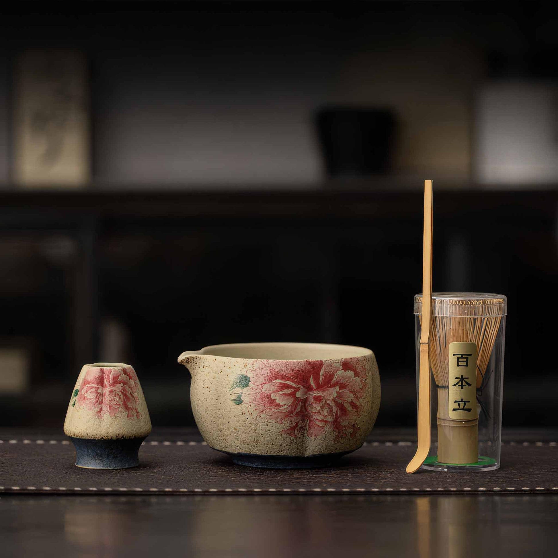 A Handcrafted matcha bowl set with a bamboo whisk and a matcha scoop, set on a dark wooden table.