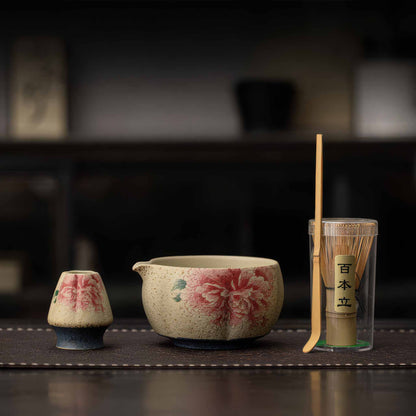 A Handcrafted matcha bowl set with a bamboo whisk and a matcha scoop, set on a dark wooden table.