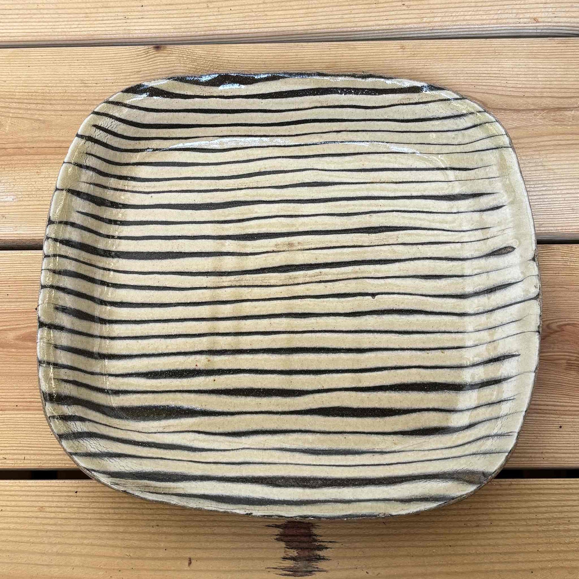 Handmade slipware square plate with hand-applied surface patterns on a wooden table.