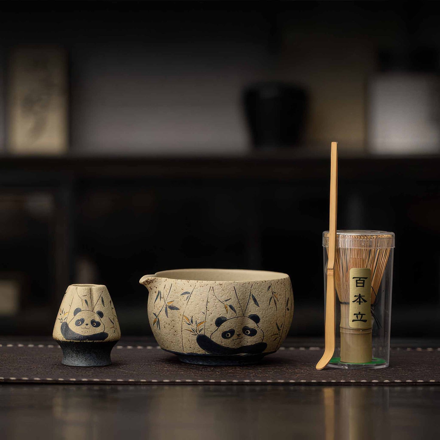 A set of handcrafted, blue and white flint red matcha bowls with accompanying bamboo whisk and tea scoop, set on a dark wooden table.
