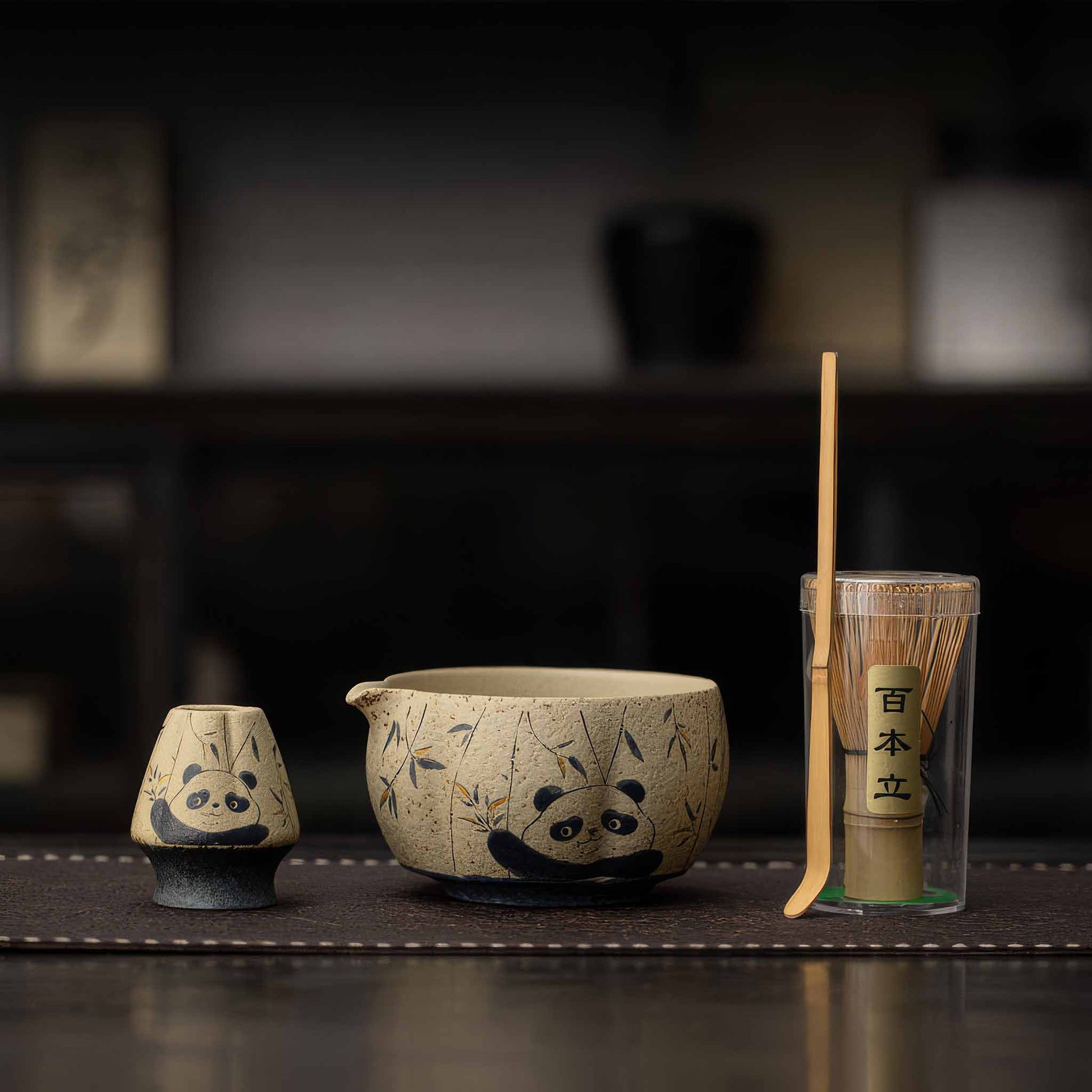 A set of handcrafted, blue and white flint red matcha bowls with accompanying bamboo whisk and tea scoop, set on a dark wooden table.