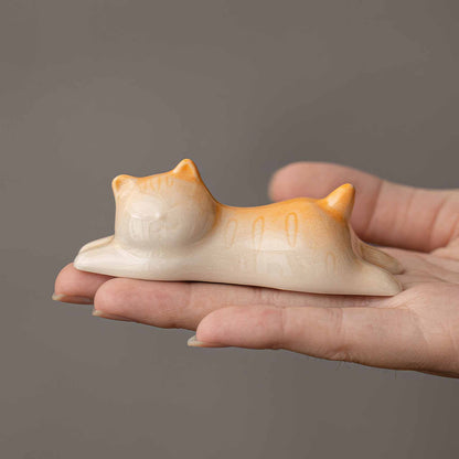 A hand holds a small, hand-painted, white and orange ceramic cat figurine.