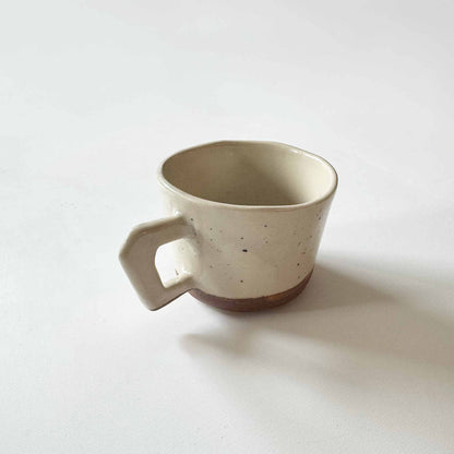 Handmade white and brown speckled ceramic espresso cup on a white surface.