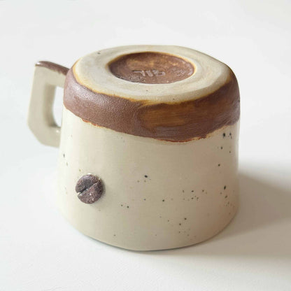 Handmade espresso cup with a cream and brown glaze, set against a neutral white background.