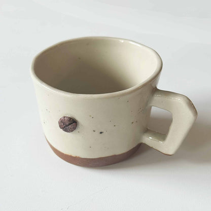 Handmade white and brown ceramic espresso cup with a small handle, set against a plain white background.