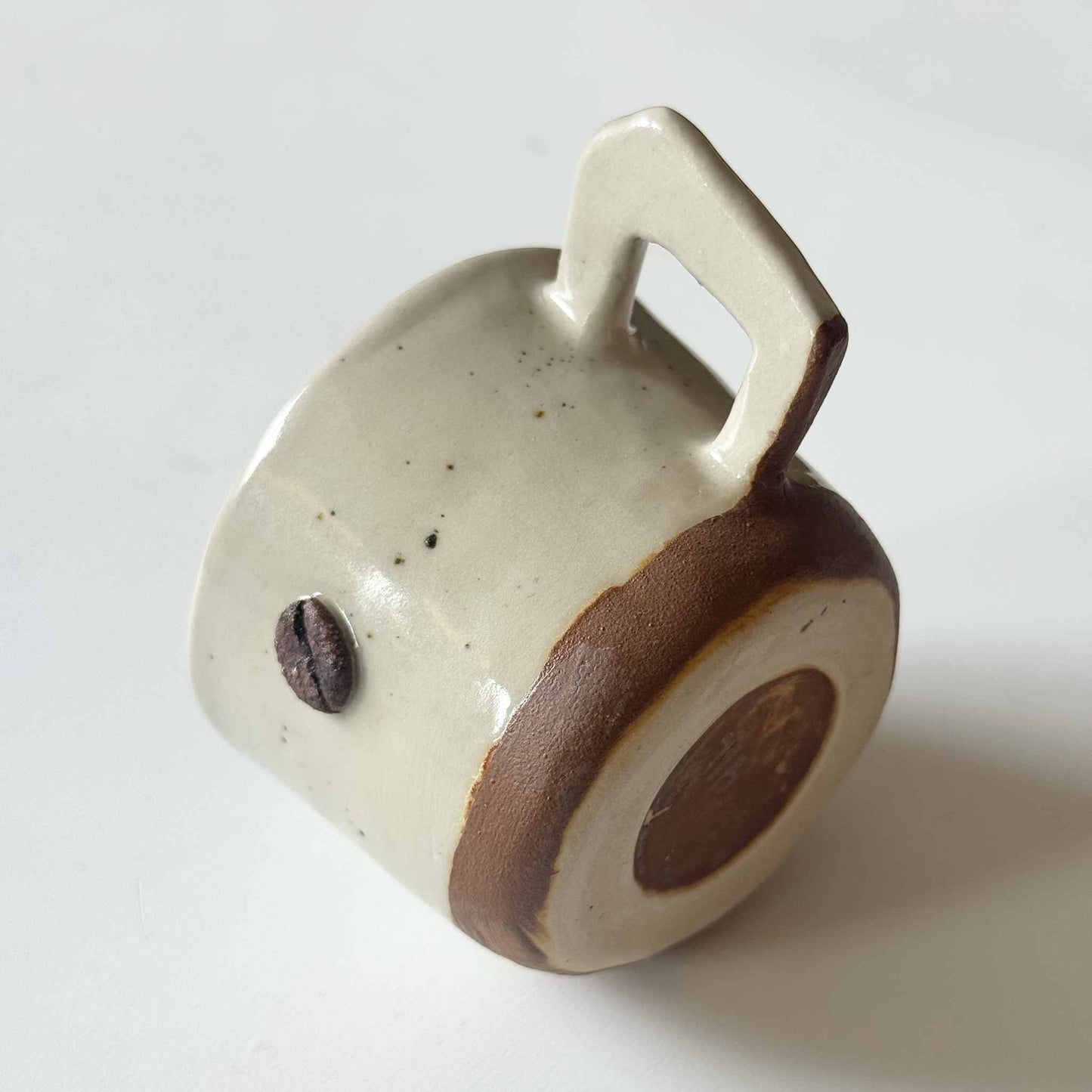 Handmade espresso cup with a white and brown glaze, placed on a white surface.
