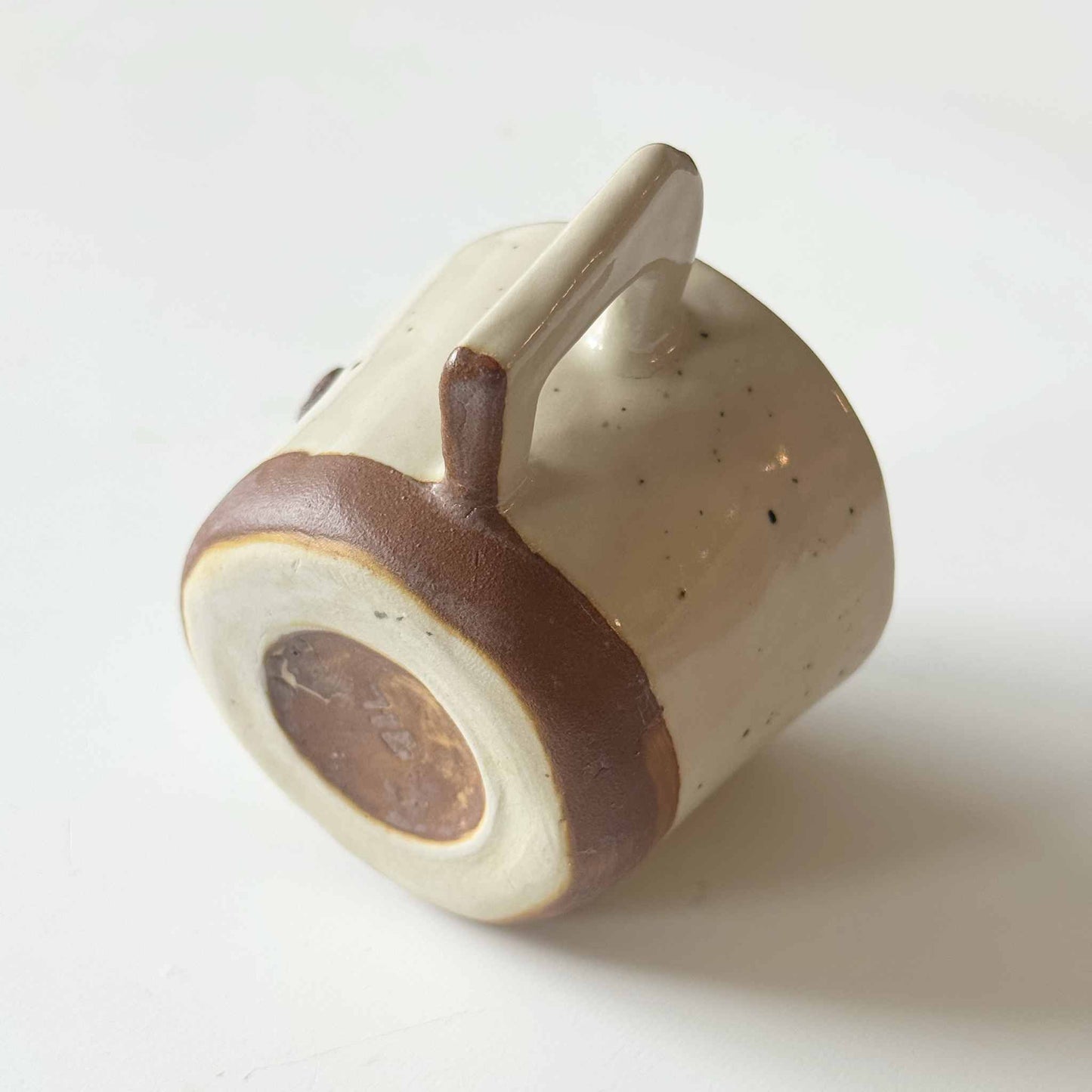 Handmade speckled white and brown ceramic espresso cup on a white surface.