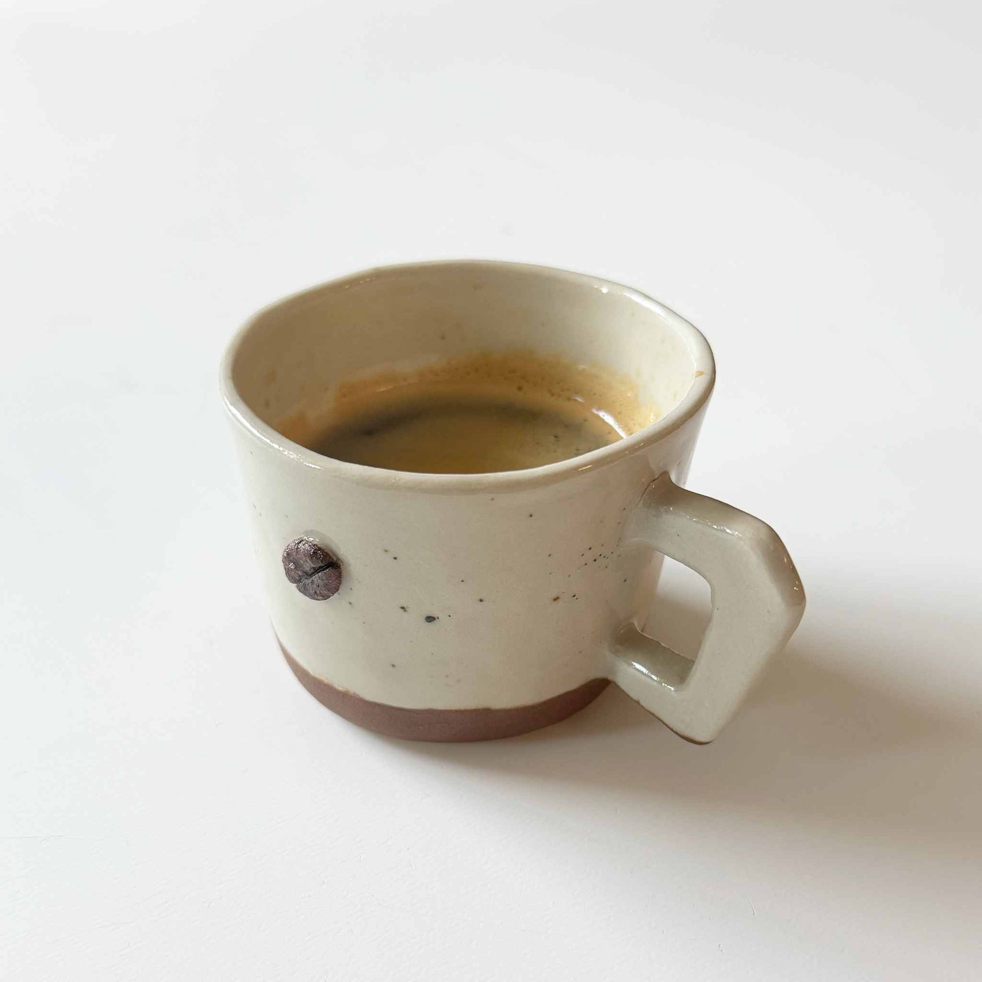 Handmade espresso cup with a white and brown speckled glaze, set against a neutral background.