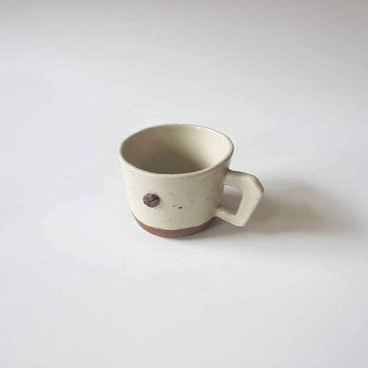 Handmade white and brown ceramic espresso cup with handle, set against a white background.
