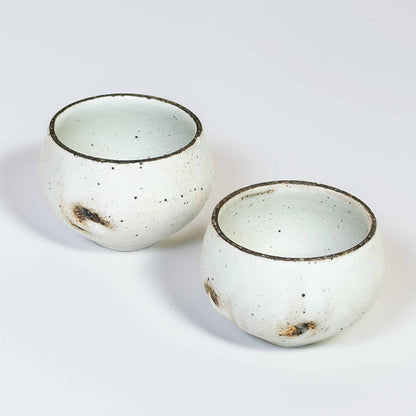 A pair of white, speckled, handcrafted soup cups with a natural glaze, set against a neutral background.