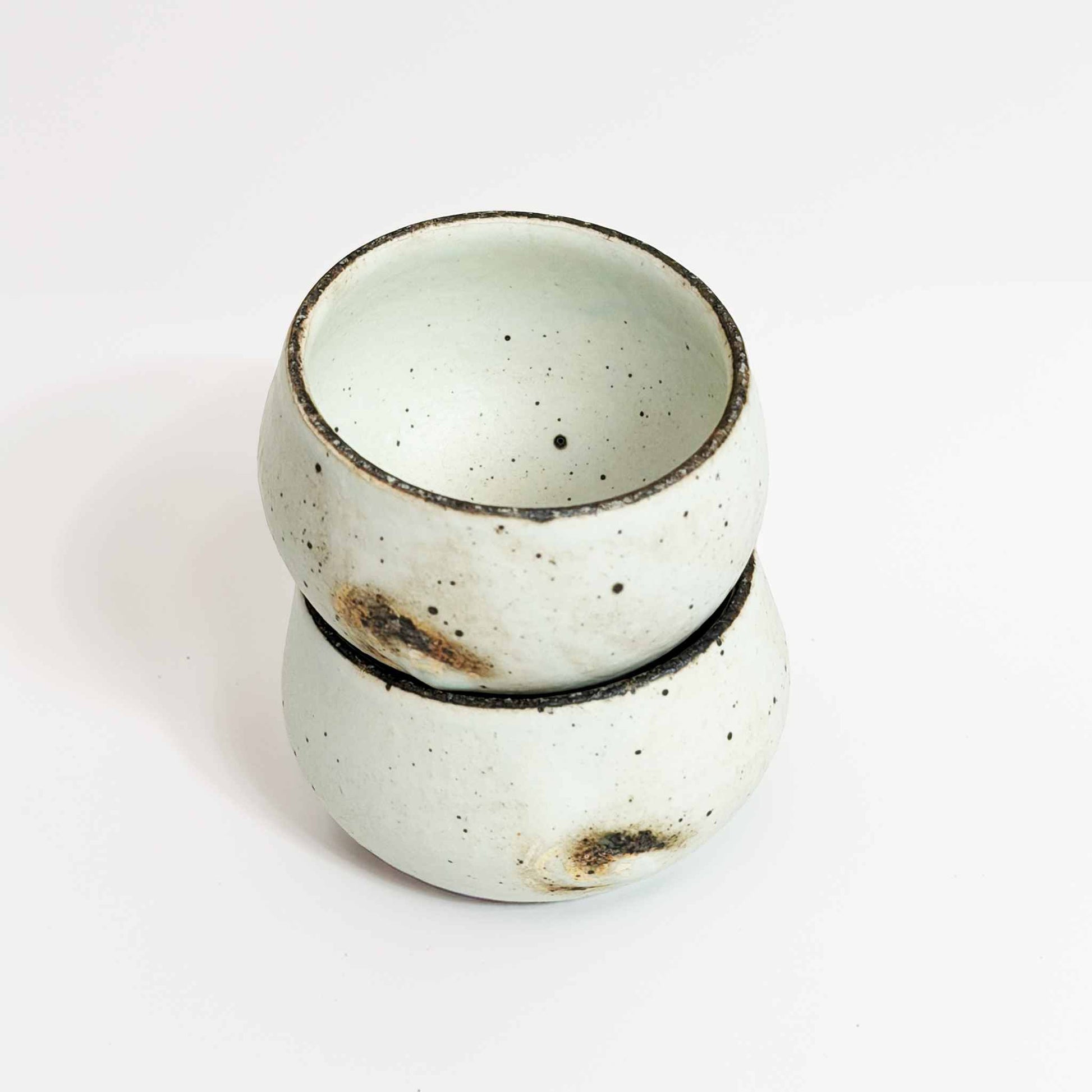 A small, handcrafted white ceramic soup cup with a natural glaze and subtle textures, set against a neutral background.