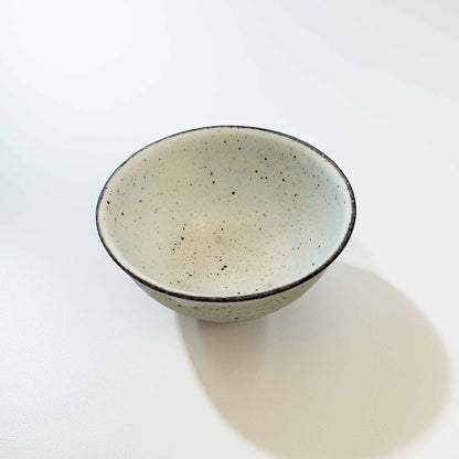 A small, white, speckled ceramic bowl with a black rim, set against a white background.