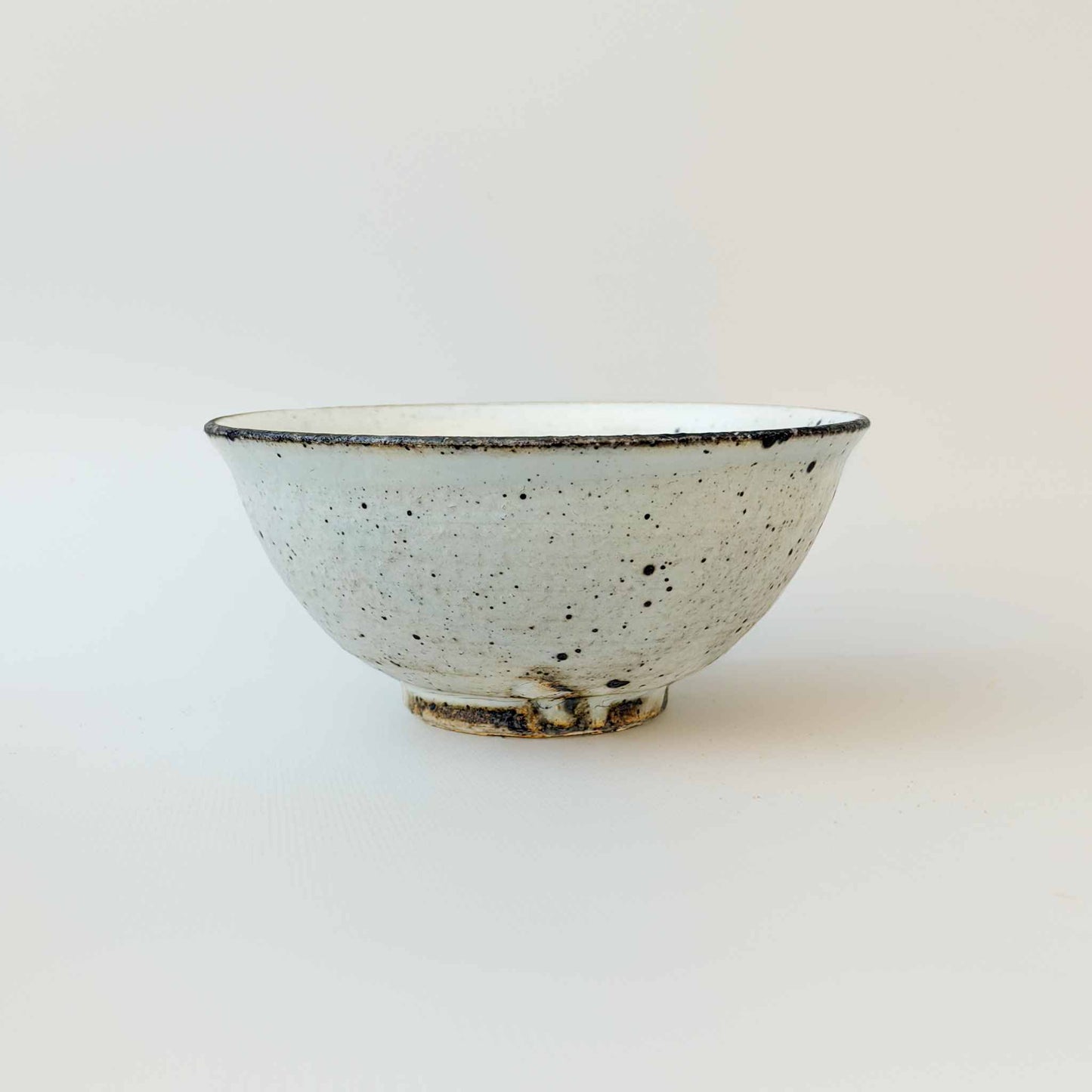 A small, white, handcrafted V-shaped bowl with a kohiki glaze, set against a plain white background.