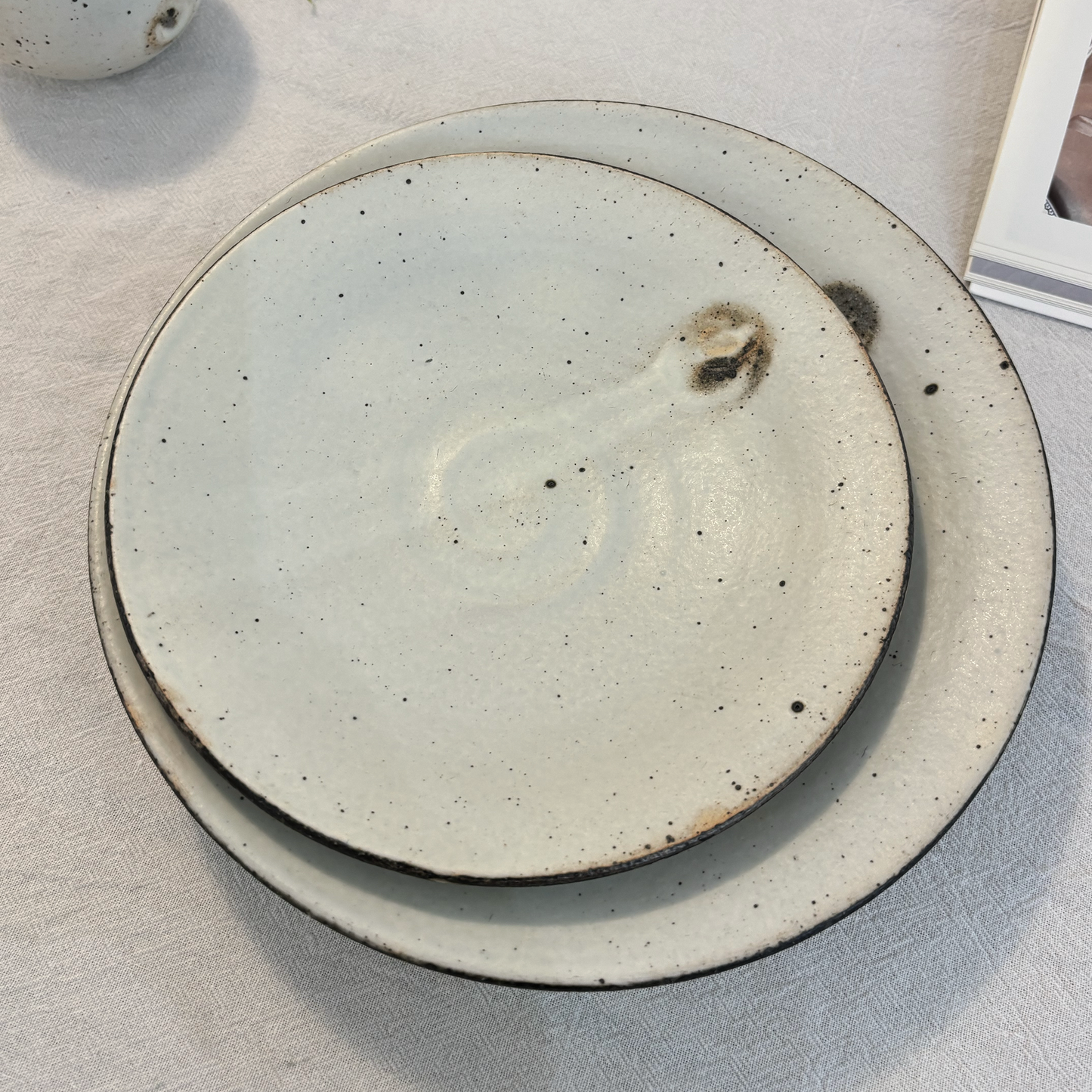 A handcrafted, shallow bowl made of ceramic material, characterized by its light gray color and speckled glaze.