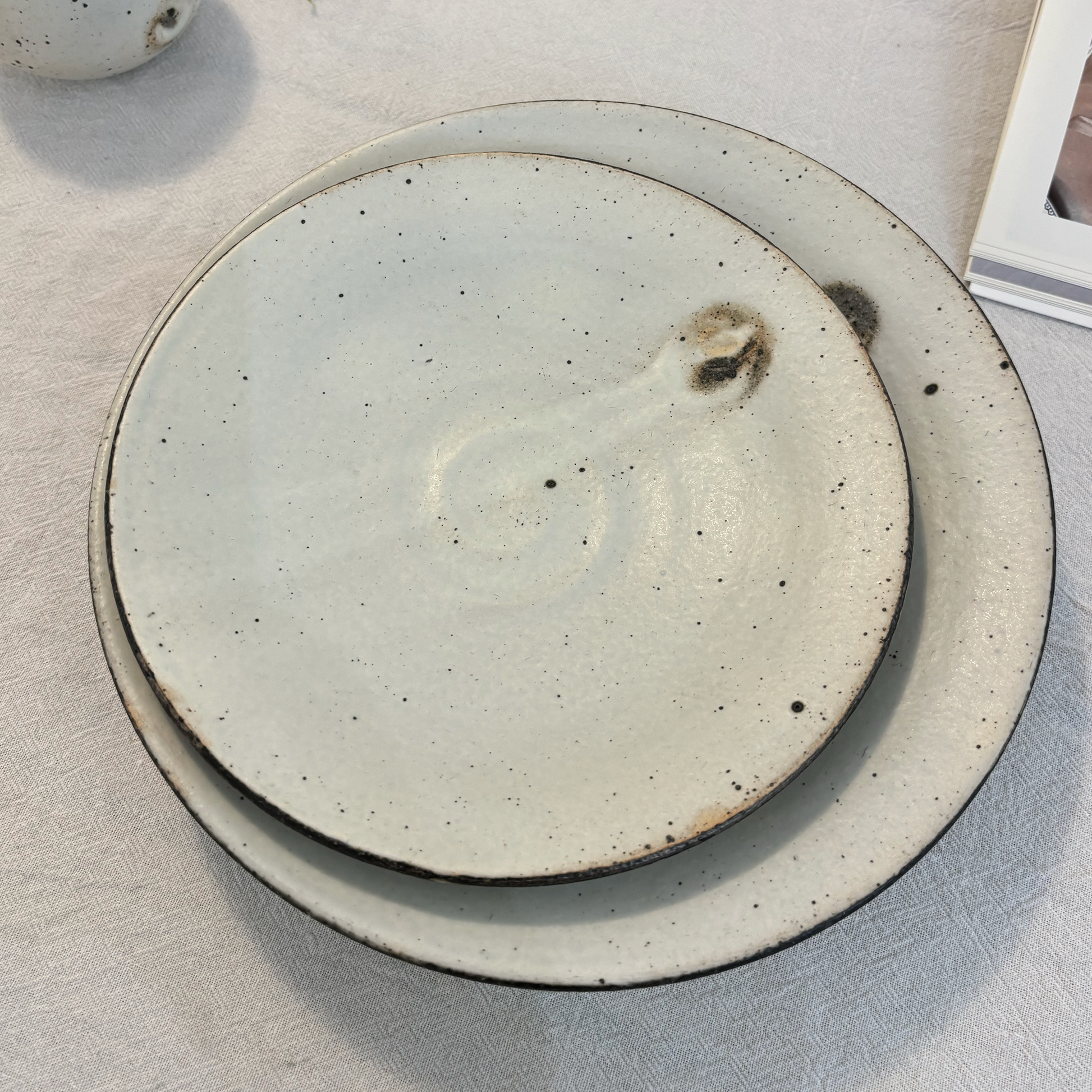 A handcrafted, shallow bowl made of ceramic material, characterized by its light gray color and speckled glaze.